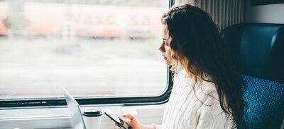 Frau sitzt auf der Fensterseite im Zug und schaut auf ihr  Handy